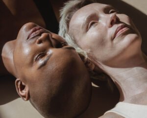 close-up of two people lying side by side with their heads resting close together under warm lighting revealing the phrase from the article the skin you think you have vs the skin you actually have