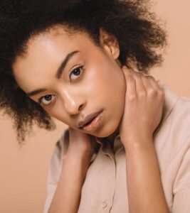 Studio portrait of a woman with curly black hair, looking directly forward while gently holding her neck