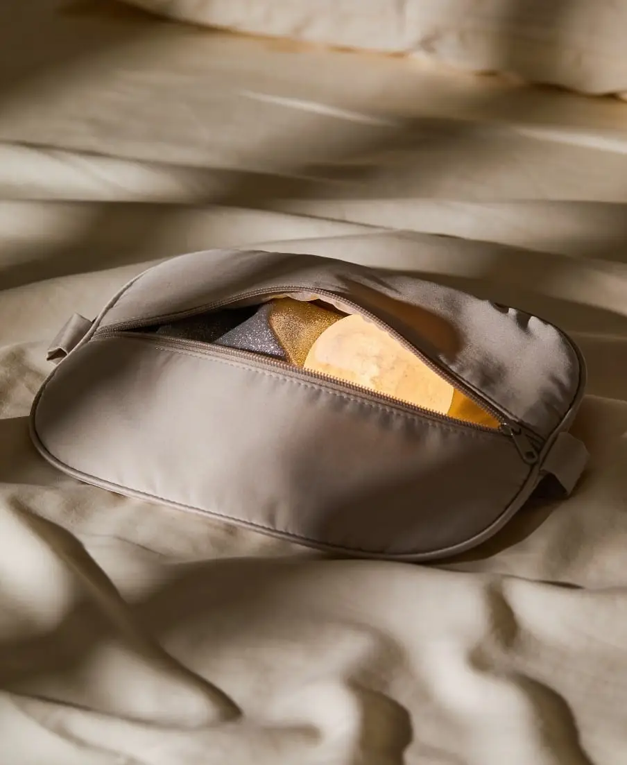 A close-up view of dark grey purse on a textured bedding, featuring a distinct, metallic gold metallic accent element resting in the purse