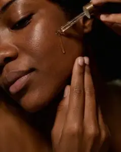 A raw, unedited, cinematic close-up of soft hands applying a liquid botanical serum directly onto a bare cheek emphasing absolute comfort