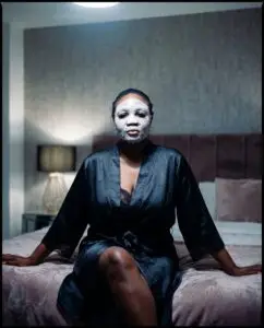 image of the founder of Saccahra with facemask on, poised elegantly in a cinematic lit bedroom, reb=veal restorative night care 