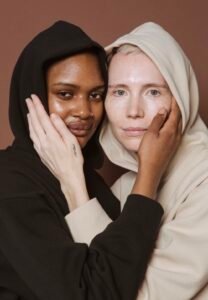 dark skin toned woman and light skin toned woman cupping each other's face showing the overlooked language of skin